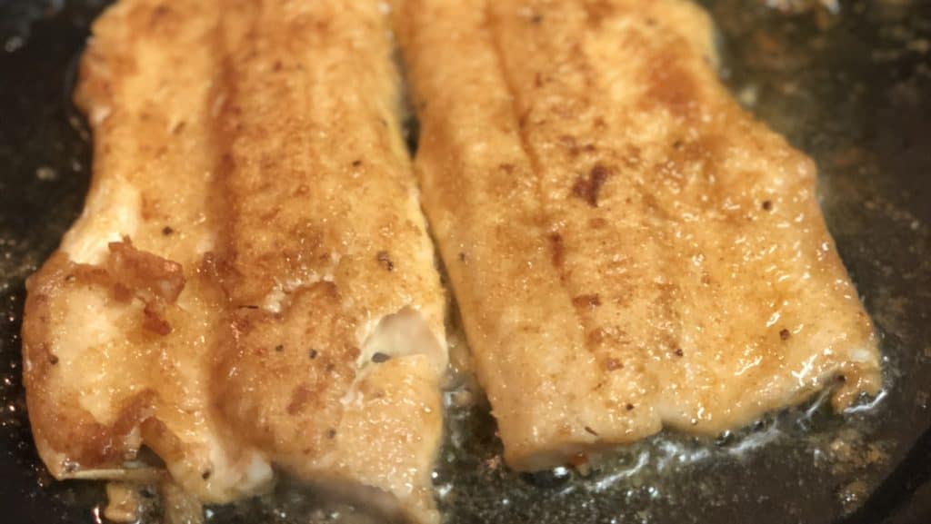 a filet of trout frying in a pan