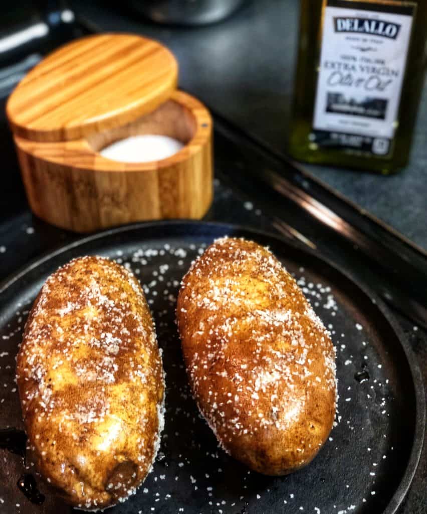 Two steakhouse baked potatoes sitting on a flat cast iron pan.