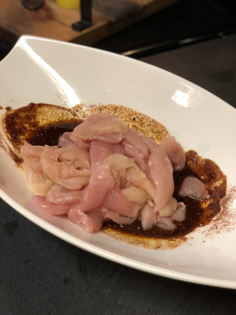 raw chicken strips marinating in a white bowl