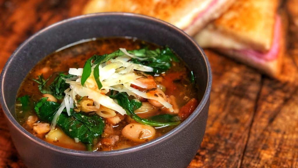 A bowl of minestrone soup with a Gruyere and Ham Grilled cheese