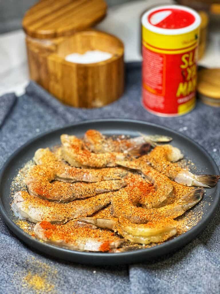 A charcoal colored plate of raw, tail-on, seasoned shrimp for Creamy Cheesy Shrimp and Grits.