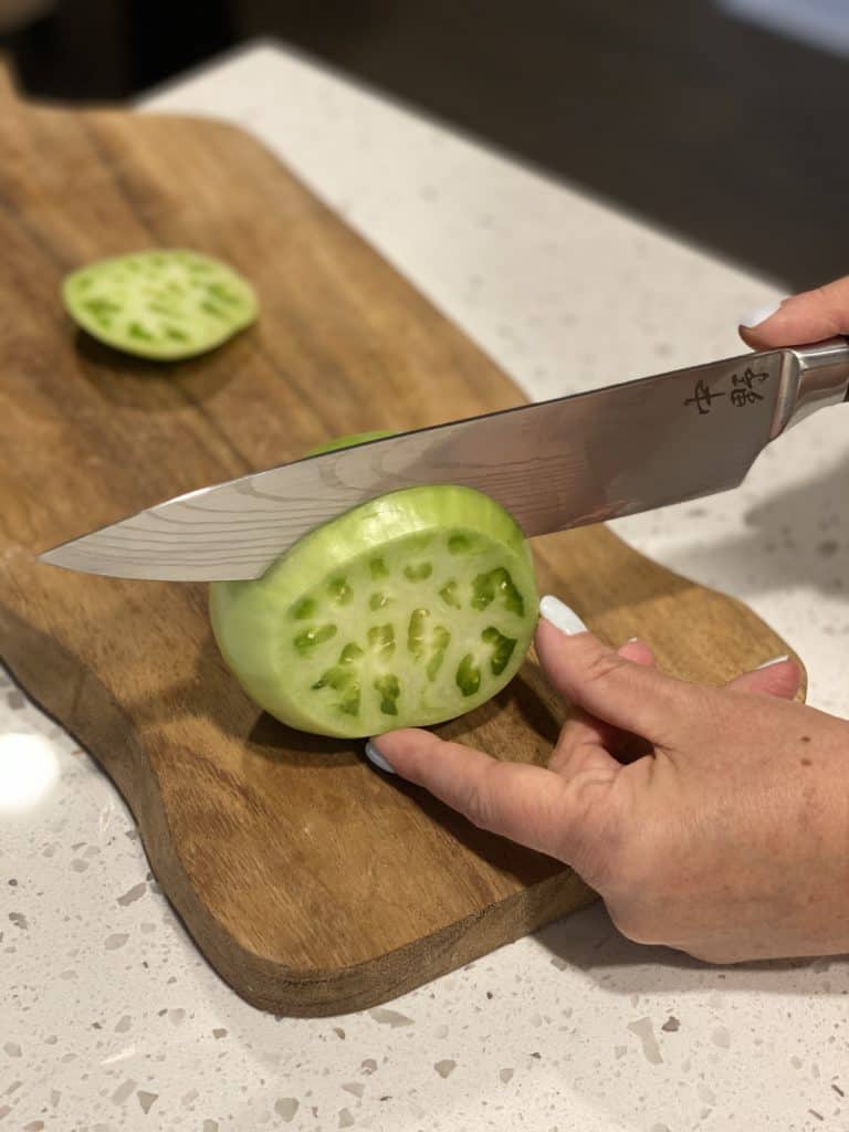 slicing up a green tomato on a wooden cutting board