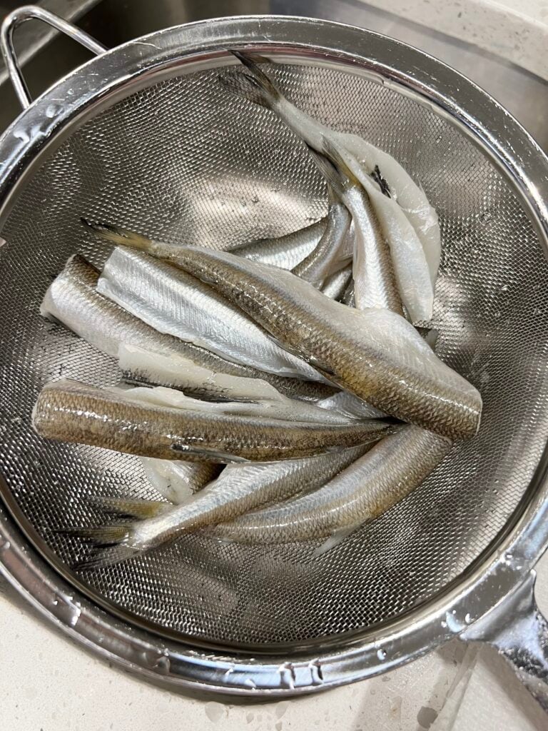 Smelt fish in a stainless steel colander. The fish are tiny.