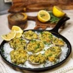 A flat cast iron pan lined with rock salt holding eight clams filled with a breadcrumb mixture. The clams have been baked.