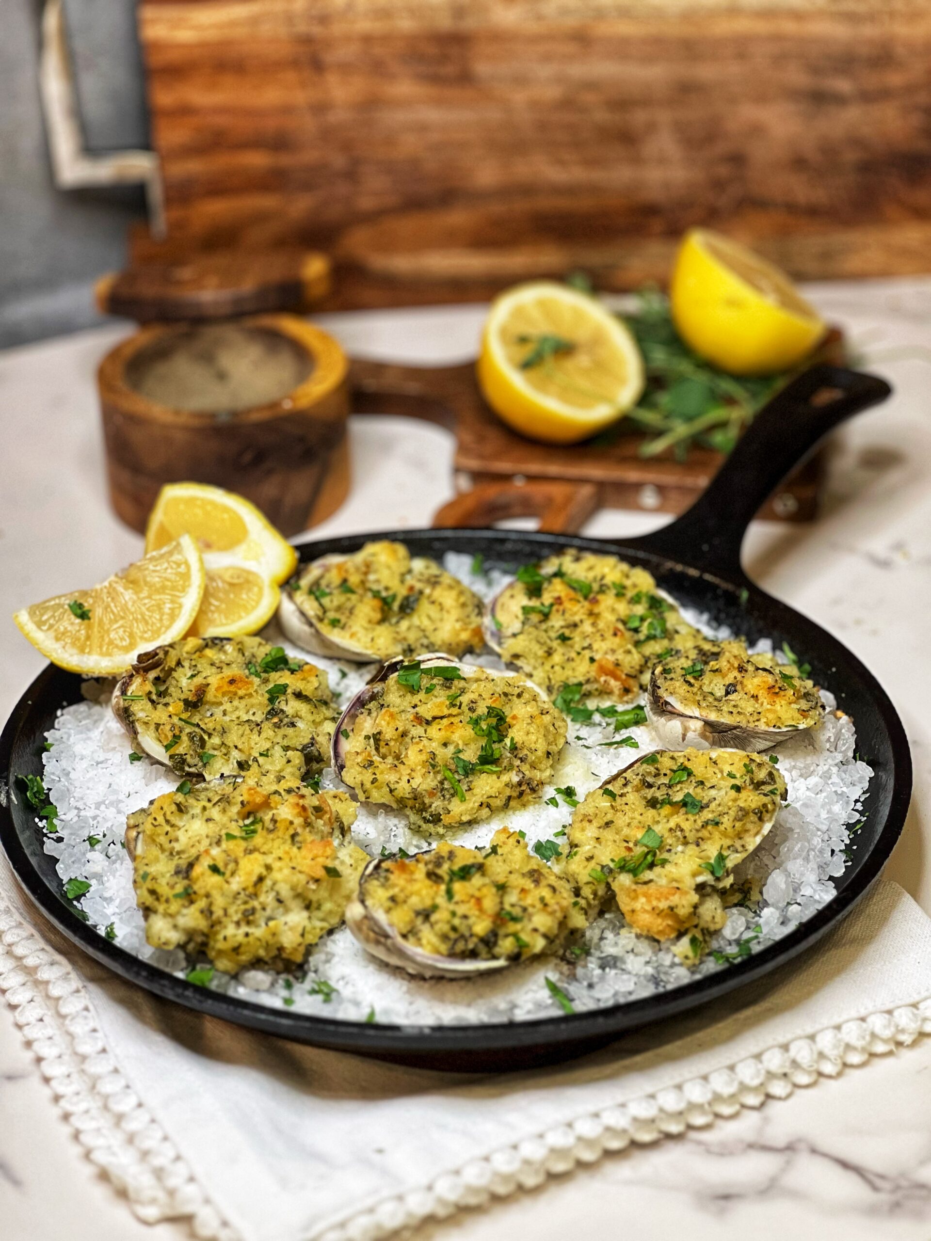 A flat cast iron pan lined with rock salt holding eight clams filled with a breadcrumb mixture. The clams have been baked.
