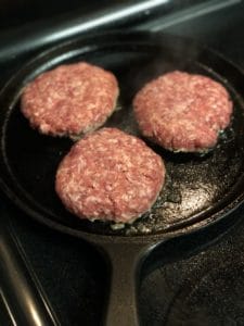three sausage patties cooking in a cast iron pan