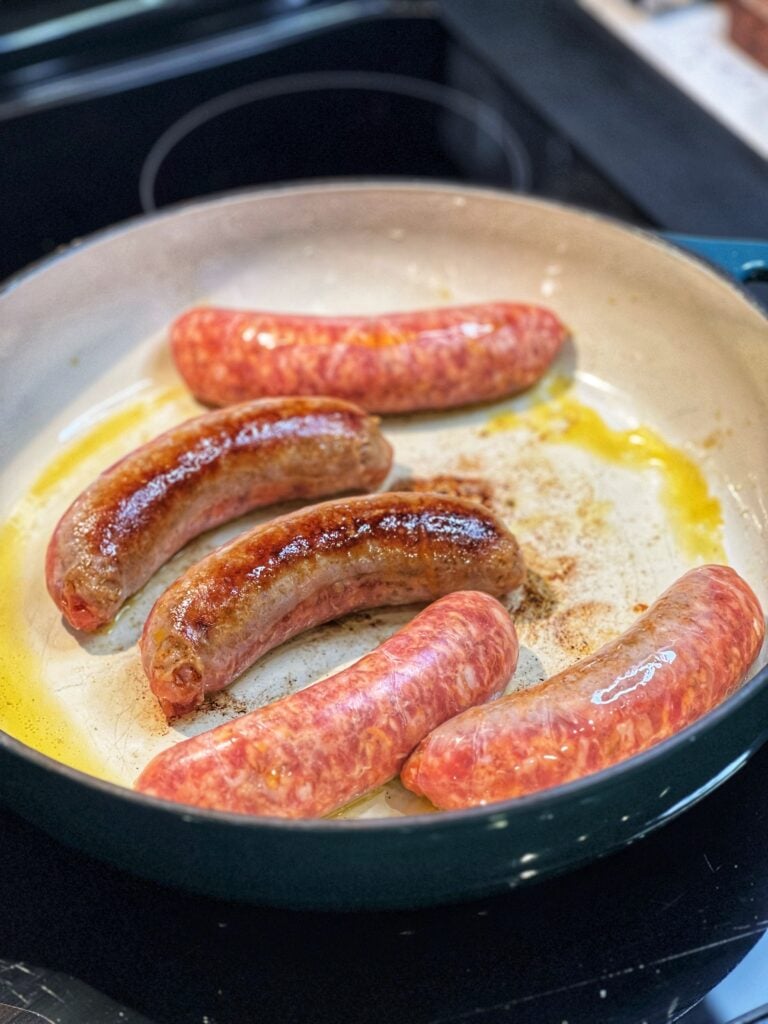 Five hot sausage links brown in an enameled cast iron pan.