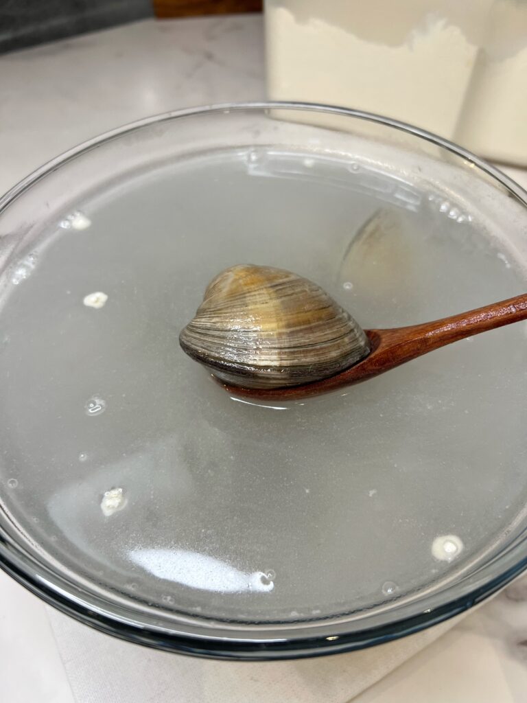 Holding a clam with a wooden spoon over a bowl of water.