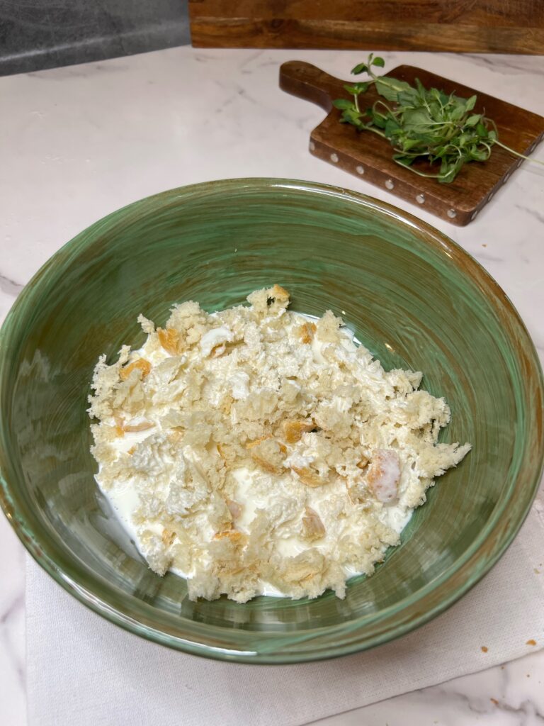 Tiny torn pieces of bread soaking in cream in a green bowl.