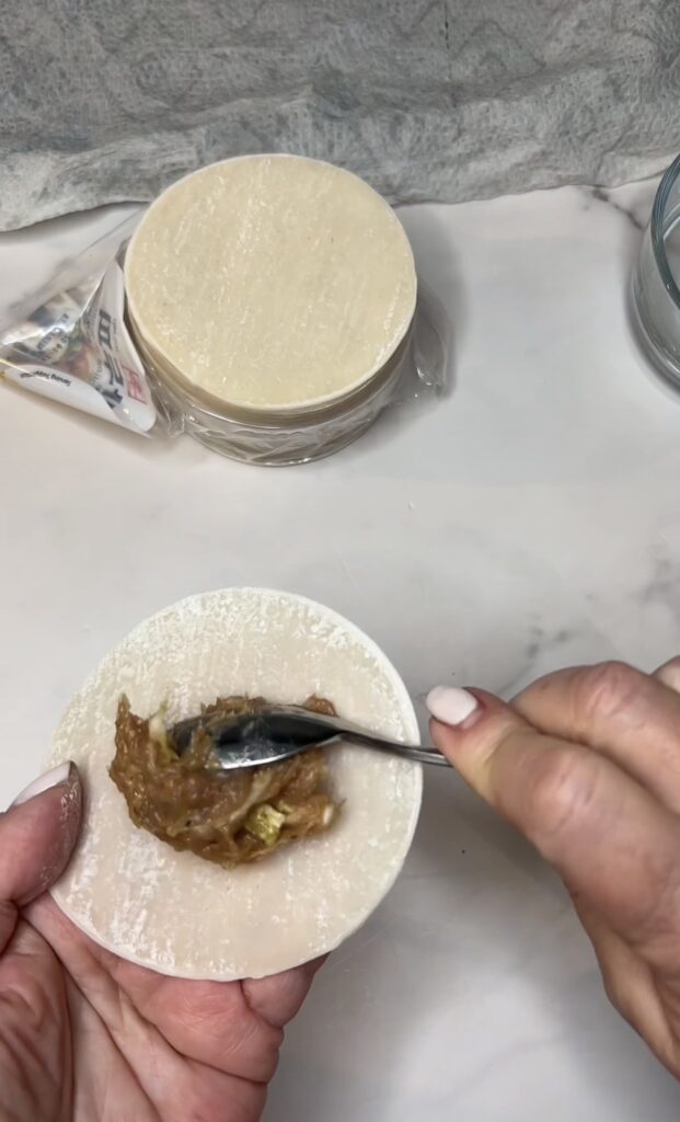 Adding a spoonful of shrimp and pork filling to the middle of a round dumpling wrapper.