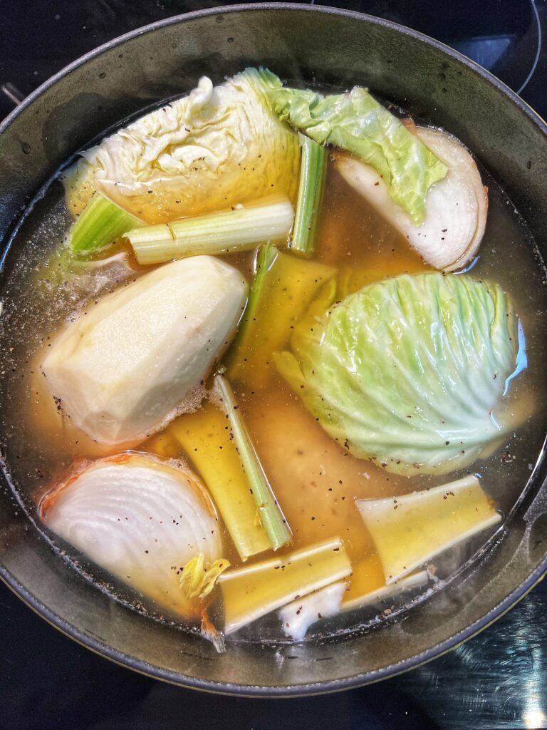 A large stock pot filled with bone-in chicken breasts, cabbage, onions, celery, potato, chicken stock and water for homemade chicken soup.