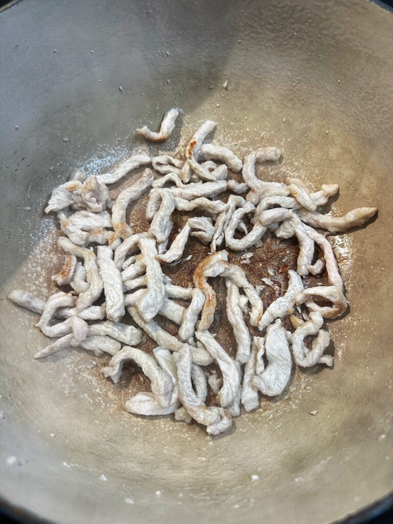 Thin strips of pork browning in a pot.