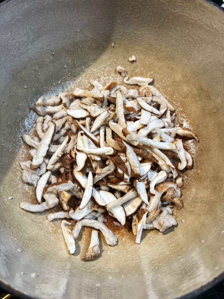 Thin strips of pork and shiitake mushrooms browning in a pot.