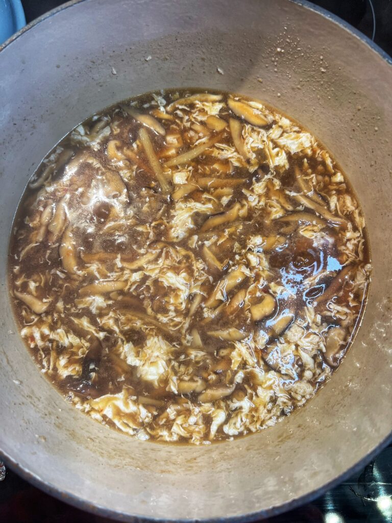 A pot of hot and sour soup. The soup is brown with mushrooms and ribbons of white egg.