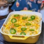 A yellow, rectangular casserole dish of chicken enchiladas topped with sour cream sauce and topped with sliced jalapeños.