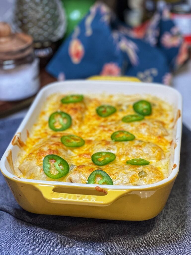 A yellow, rectangular casserole dish of chicken enchiladas topped with sour cream sauce and topped with sliced jalapeños.