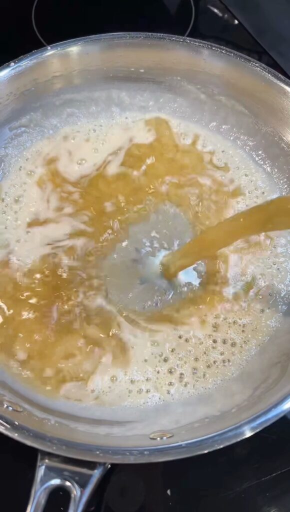 Pouring chicken stock in a pan of a flour and butter mixture.