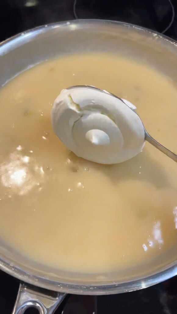 Adding a spoonful of sour cream into a thick sauce for chicken enchiladas.
