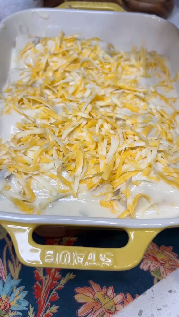 A yellow casserole dish filled with chicken enchiladas that have been topped with a sour cream sauce and shredded cheese.