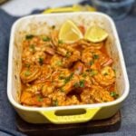 A small, yellow rectangular casserole dish filled with angry shrimp. The shrimp are baked in a spicy sauce and garnished with fresh parsley and served with lemon wedges.