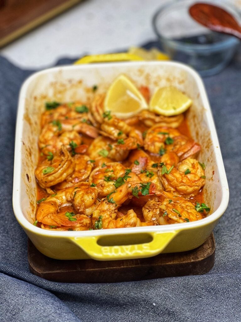 A small, yellow rectangular casserole dish filled with angry shrimp. The shrimp are baked in a spicy sauce and garnished with fresh parsley and served with lemon wedges.