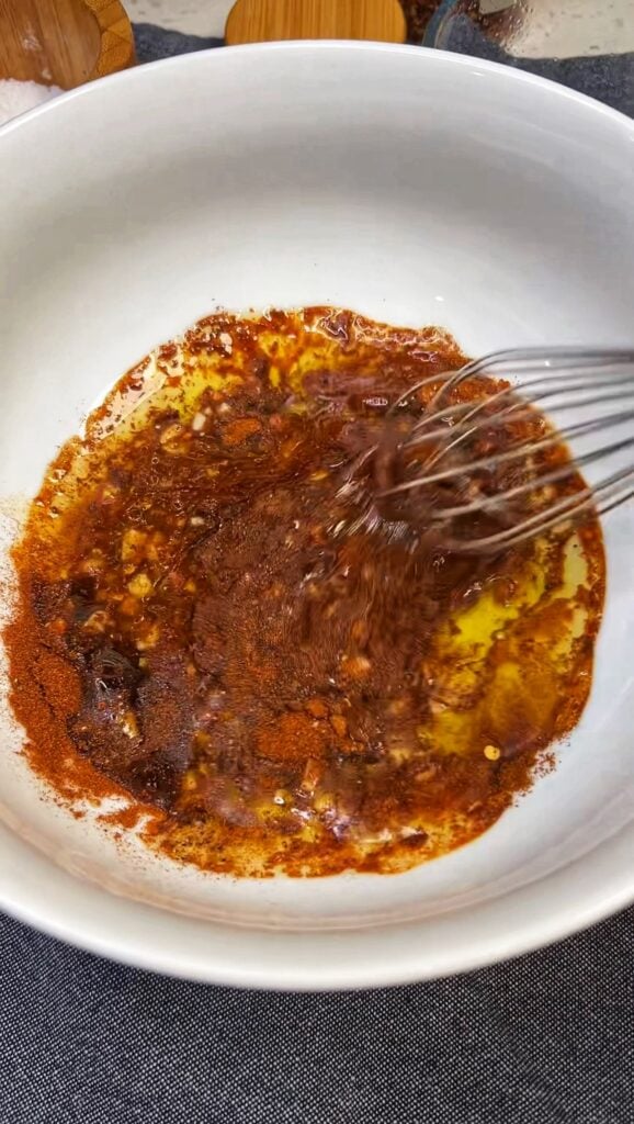 Whisking olive oil, paprika, lemon juice, and minced garlic to make a sauce for angry shrimp.