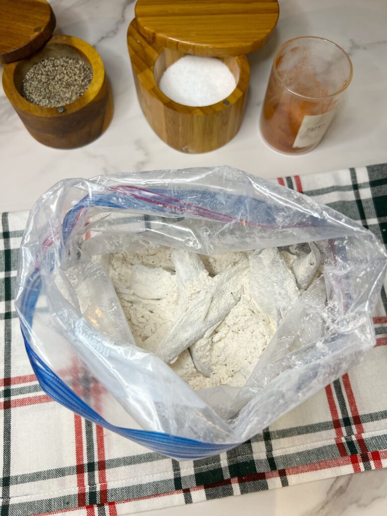 Dredging smelt fish in a freezer bag filled with a seasoned flour mixture.