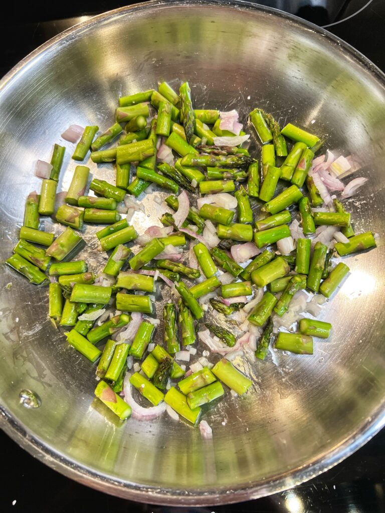 Sautéing cut asparagus and shallots in a sauté pan.