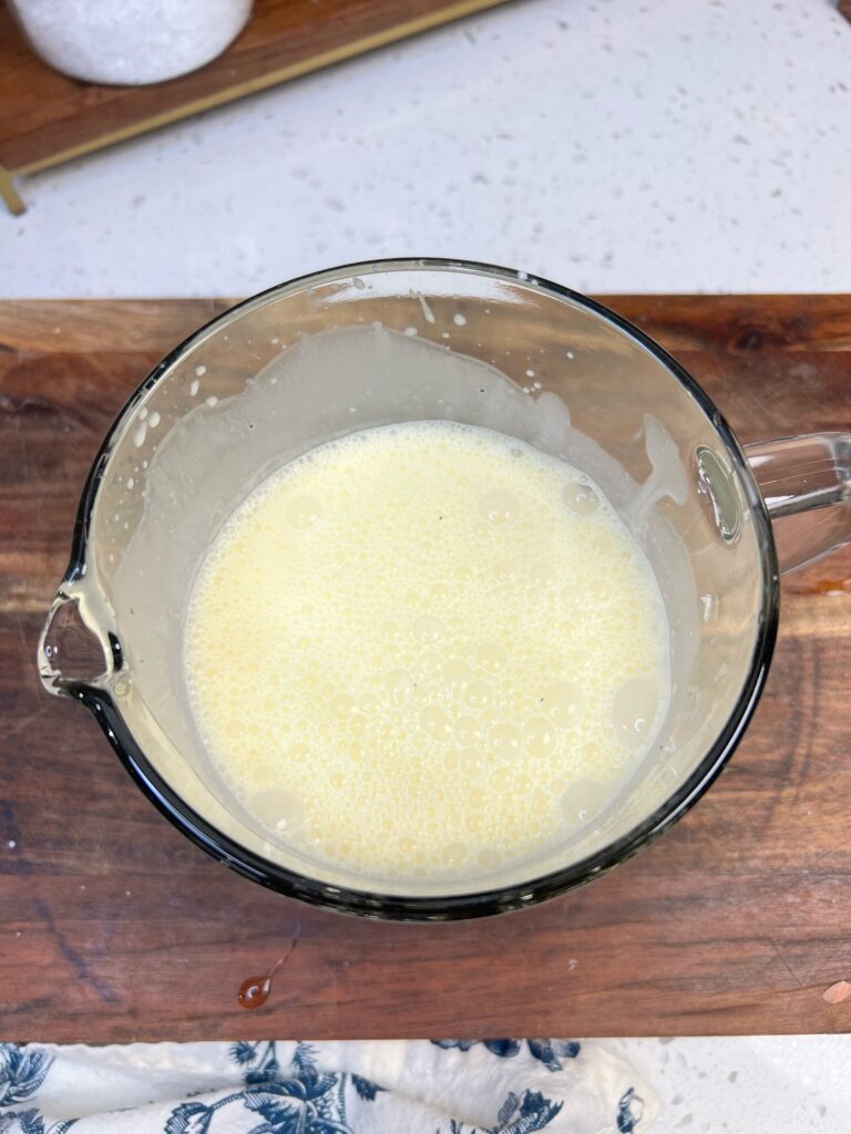 An egg cream mixture in a large glass measuring cup for quiche.