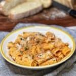 A round white bowl trimmed in yellow filled with rigatoni covered in a spicy sausage cream sauce and garnished with freshly grated Parmesan cheese.