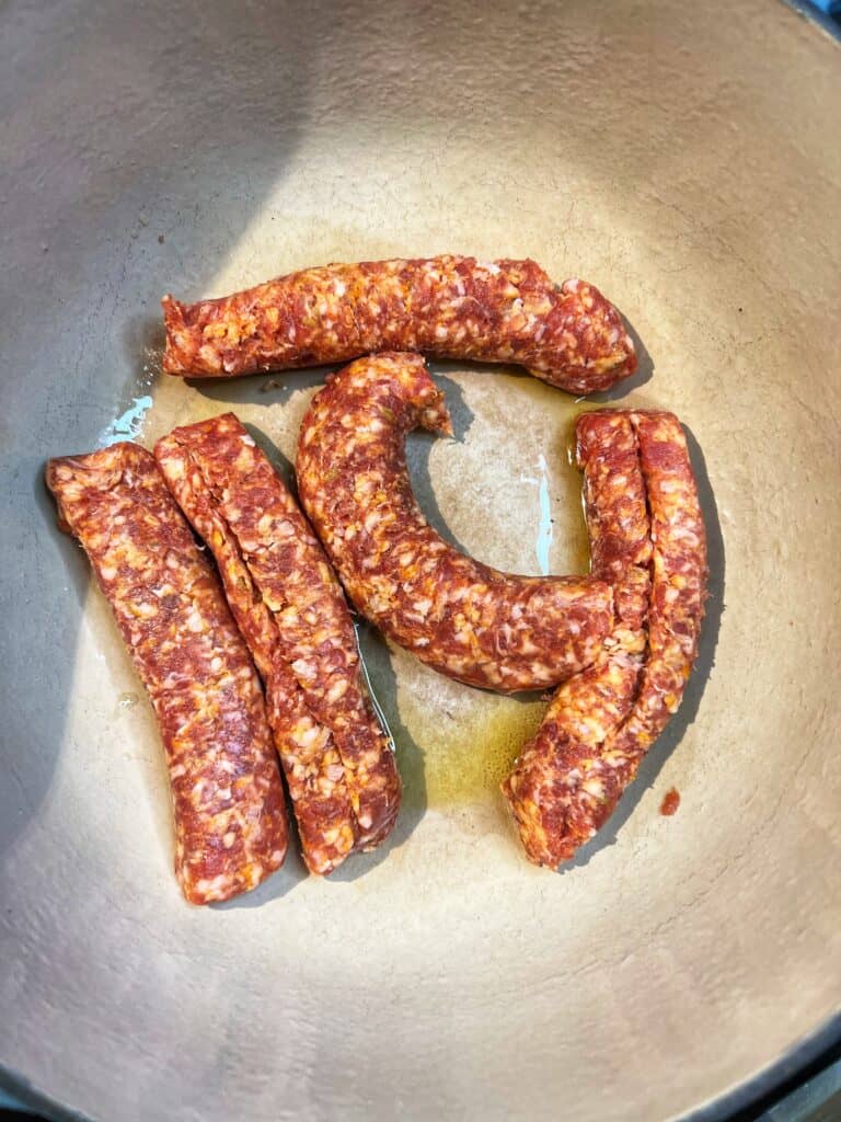 Five hot sausage links with their casings removed in a large pot with olive oil.
