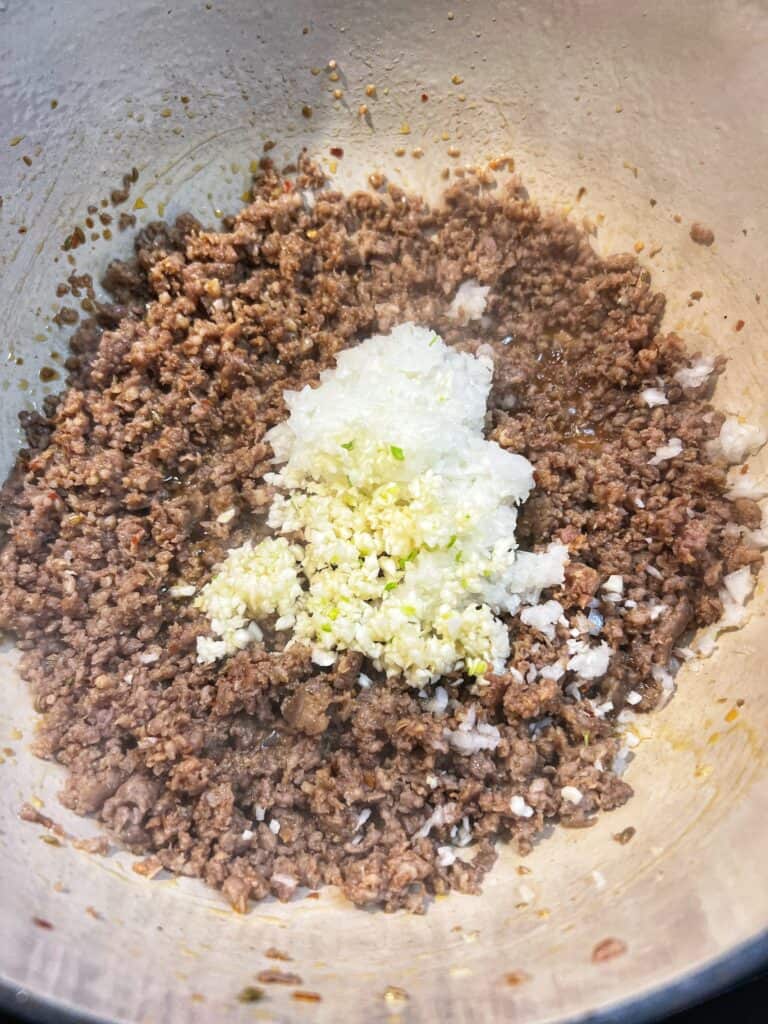 Minced onions and garlic added to a pot of ground hot sausage.