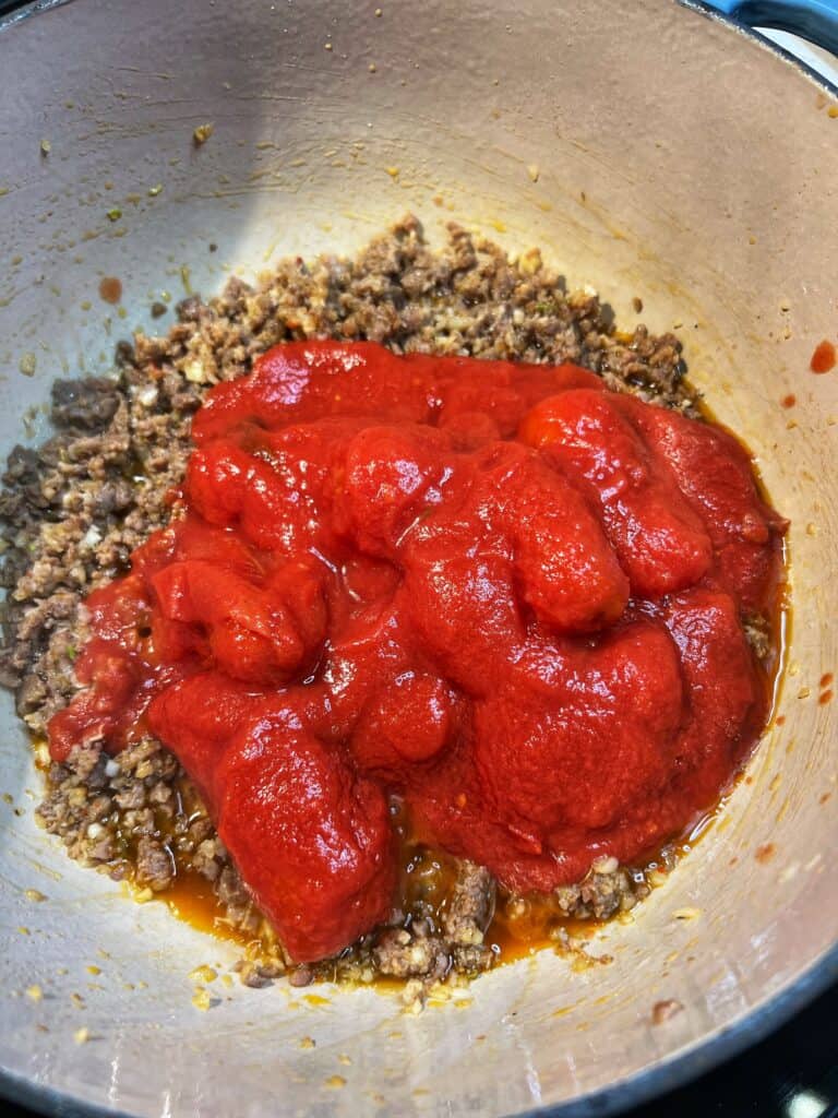 Whole tomatoes in a pot with ground hot sausage.