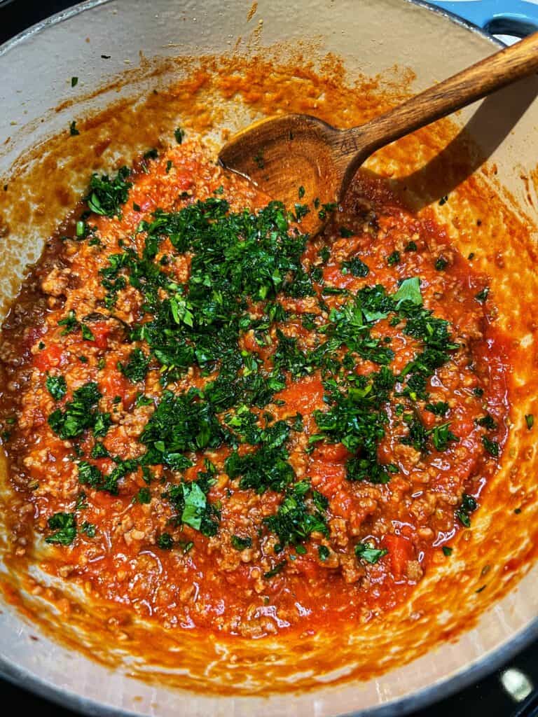 Fresh chopped parsley added to a pot of spicy sausage tomato sauce.