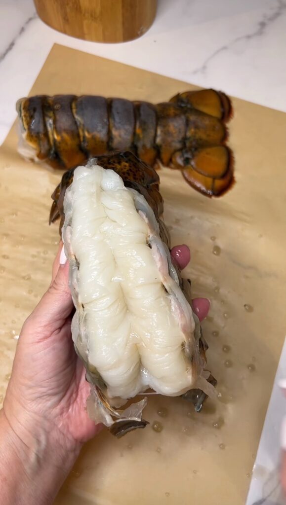 A raw lobster tail meat taken out of it's shell from the top and placed on top of the shell. 