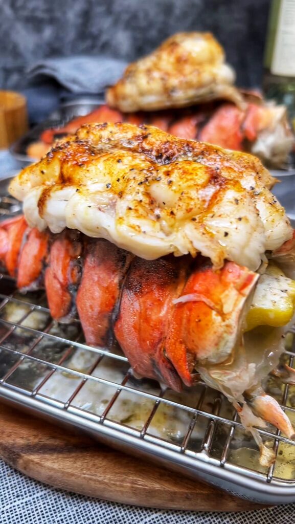 A broiled lobster tail that has been broiled with seasonings and butter. The meat is sitting on the shell and is slightly browned in color from the butter.
