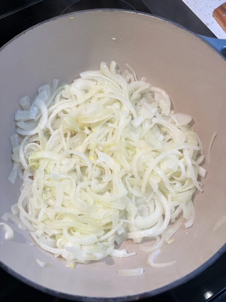 Sliced yellow onions sautéing in a pot.