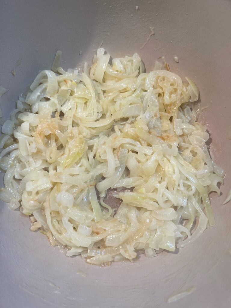 Sliced yellow onions starting to caramelize in a pot.