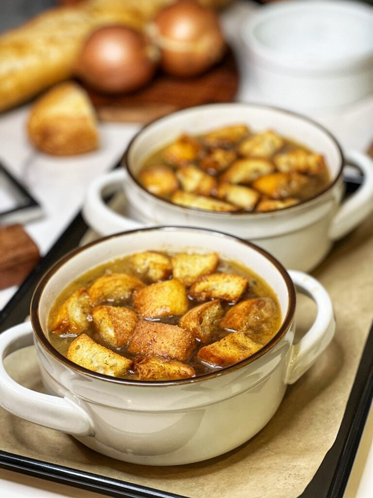 Two white soup crocks filled with French onion soup and croutons.