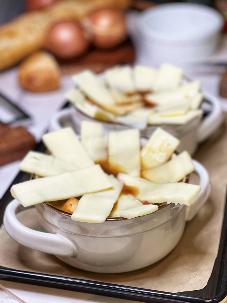 Two white soup crocks holding French onion soup and topped with sliced white cheese.