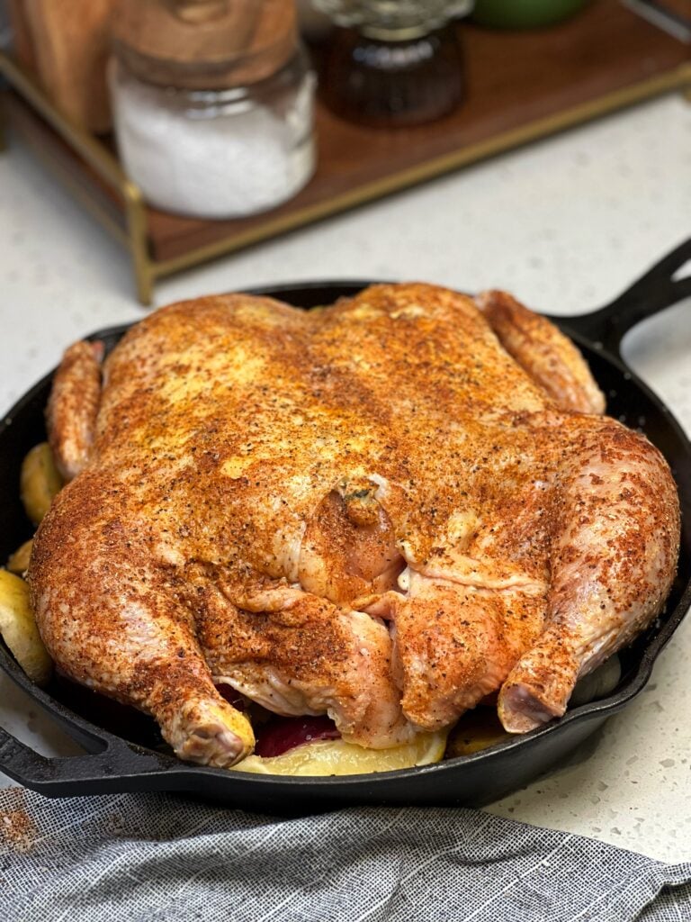 A seasoned spatchcock chicken sitting on top of vegetables in a cast iron pan.