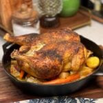 A roasted spatchcock chicken in a cast iron pan. The chicken is flat and golden brown and is laying on top a bed of roasted vegetables.