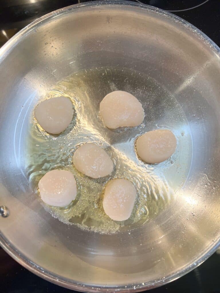 Five scallops searing in a stainless steel pan.