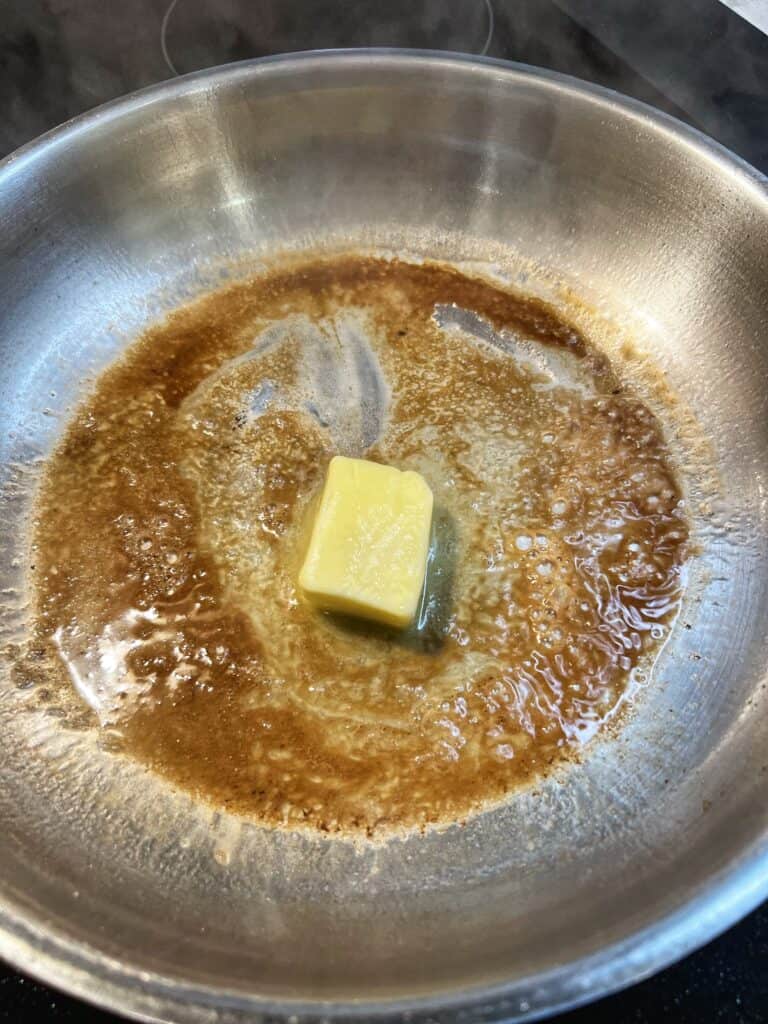 Butter added to a stainless steel pan with drippings from searing scallops.