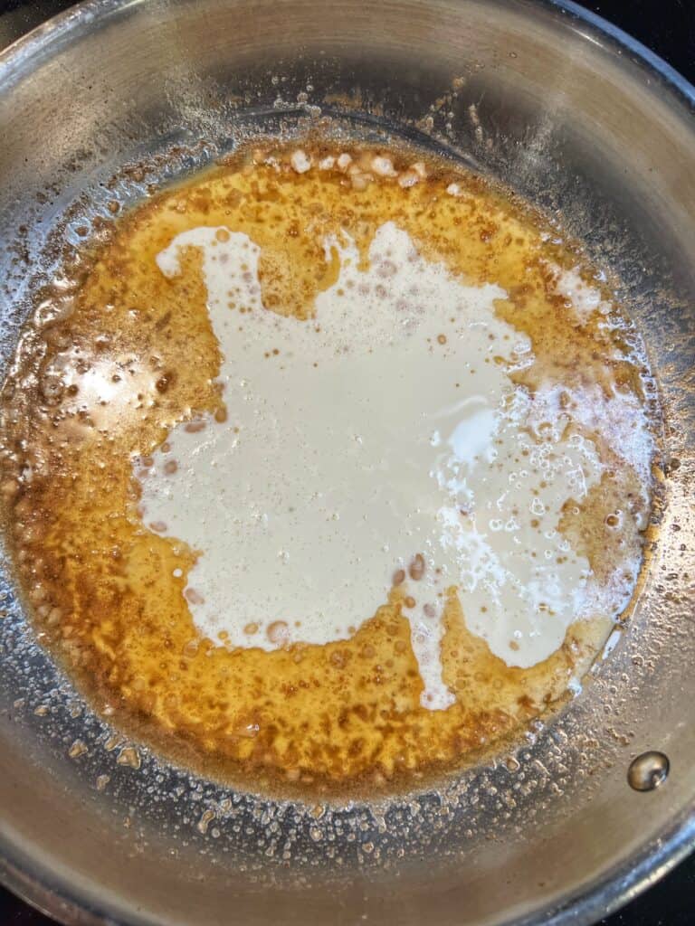 Heavy cream added to a stainless steel pan with butter and minced garlic.