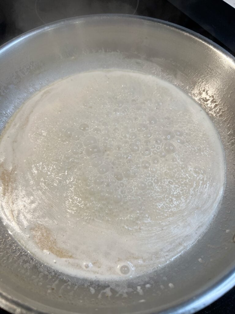 Cream sauce simmering hard in a stainless steel pan.