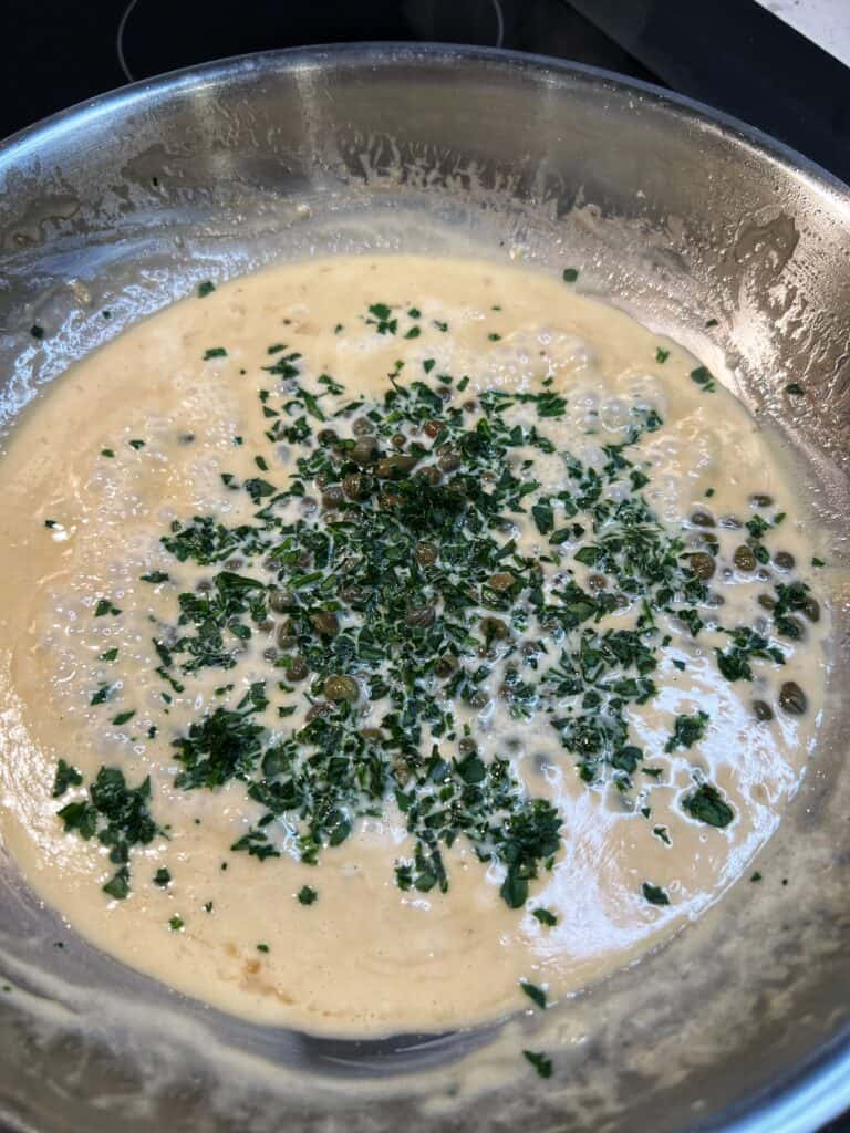 Creamy Lemon Butter Caper Sauce waiting to be stirred in a stainless steel pan.