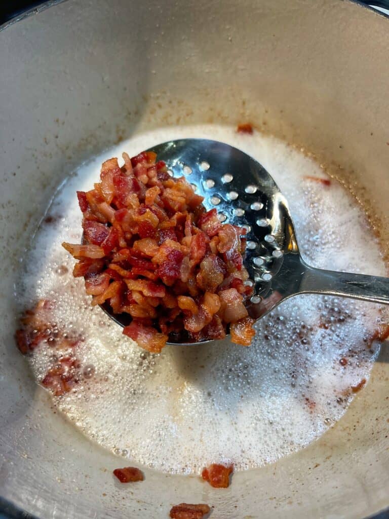 Crisp diced bacon on a slotted, stainless steel spoon.