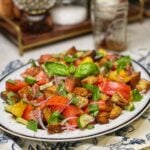 A fresh Panzanella salad with heirloom tomatoes, sliced red onion, croutons, cucumbers and fresh basil on a white platter.