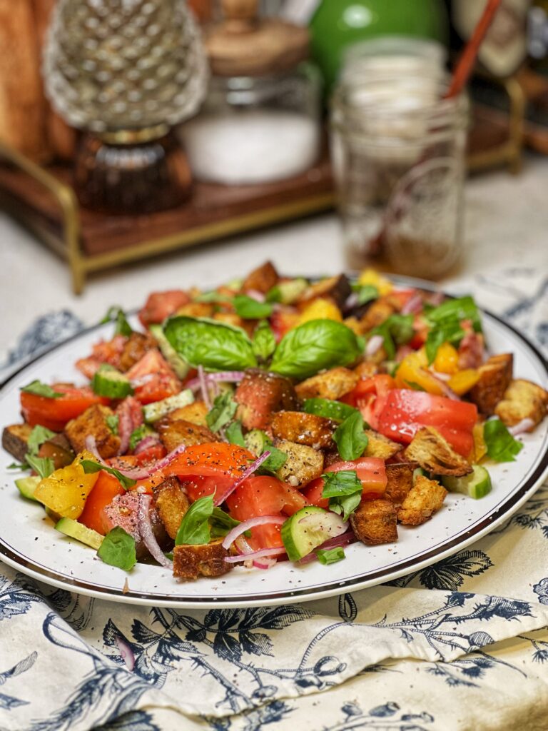 A fresh Panzanella salad with heirloom tomatoes, sliced red onion, croutons, cucumbers and fresh basil on a white platter.